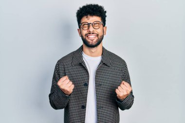 Sakallı genç Arap adam başarı için heyecanlanıyor kolları havada ve gözleri kapalı zaferi kutluyor. Kazanan konsept. 