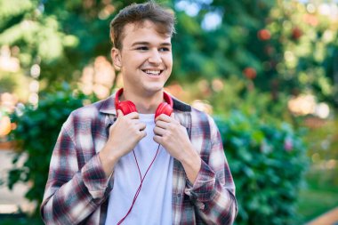 Parkta kulaklık takıp gülümseyen beyaz bir genç..