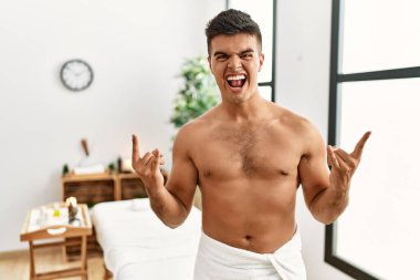 İspanyol asıllı genç adam spa merkezinde üstsüz duruyor çılgın bir ifadeyle bağırıyor elleri havada rock sembolü yapıyor. Müzik yıldızı. ağır kavram. 