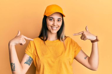 Teslimat üniforması ve şapkası giyen genç İspanyol kadın. Yüzünde bir gülümsemeyle kendinden emin görünüyor. Kendini gururlu ve mutlu bir şekilde gösteriyor.. 