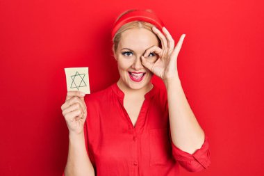 Sarışın genç bir kadın elinde Yahudi yıldızı hatırlatıcısı gülümsüyor mutlu bir şekilde el pençe divan duruyor. 