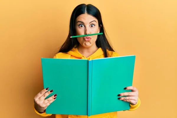 stock image Funny hispanic woman reading a book doing crazy gesture with pencil over mouth like mustache, playful and positive on free time, lazy student