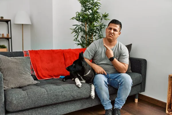 Jovem Latino Cão Sentado Sofá Casa Apontando Para Lado Preocupado — Fotografia de Stock