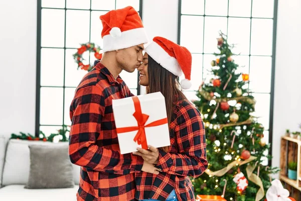 Young Latin Couple Holding Gift Standing Christmas Tree Home — Stock Photo, Image