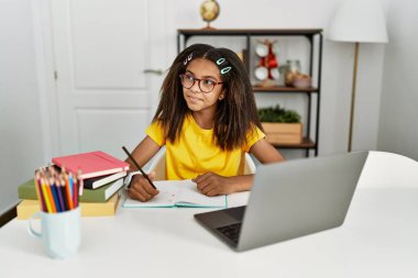 Genç Afrikalı Amerikalı kız evde ödev yapıyor. Gülümsüyor, yan tarafa bakıyor ve düşünüyor.. 