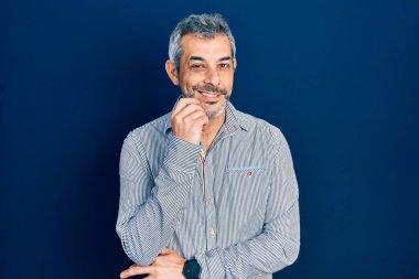 Gri saçlı yakışıklı, iş gömleği giyen, kameraya kendinden emin, kolları çapraz ve çenesi açık gülümseyen bir adam. Olumlu düşünmek. 