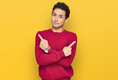 Her iki tarafı parmaklarıyla gösteren gündelik giysiler giyen genç yakışıklı adam farklı yönlere bakıyor. 