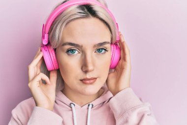 Kulaklıkla müzik dinleyen genç sarışın kız yüzünde ciddi bir ifadeyle rahatlamış. Basit ve doğal bir şekilde kameraya bakıyorsun.. 