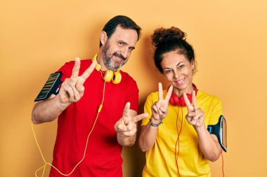 Orta yaşlı bir çift İspanyol kadın ve spor kıyafetleri ve kol bandı takmış parmaklarını zafer işareti yaparken gösteren kameraya gülümseyen bir adam. İki numara.. 