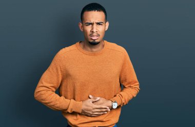 Afro-Amerikalı genç bir adam, hazımsızlık, acı verici bir hastalık ve midesi üzerine gündelik giysiler giyiyor. Ağrı kavramı. 