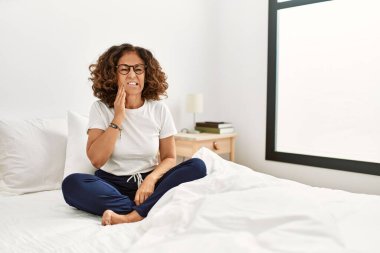 Orta yaşlı İspanyol bir kadın diş ağrısı ya da diş hastalığından dolayı evde yatağında ağzıyla acı dolu bir ifadeyle dokunuyor. dişçi 