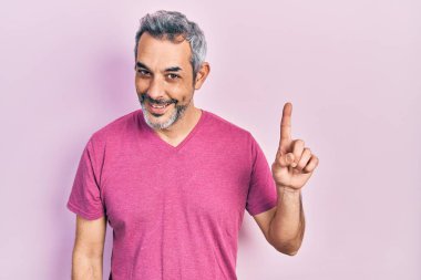 Gri saçlı, sıradan pembe tişörtlü yakışıklı bir adam bir fikir veya soruyla gülümsüyor ve mutlu bir yüzle işaret ediyor. 