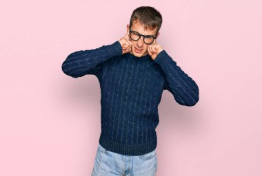 Gürültülü müzik sesi için günlük kıyafetler giyen ve kulaklarını parmaklarıyla kapatan genç sarışın bir adam. sağır kavramı. 