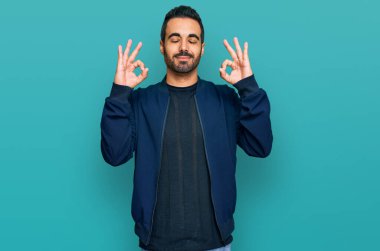 Günlük kıyafetler giyen genç İspanyol adam rahatla ve gözleri kapalı gülümse parmaklarıyla meditasyon hareketi yapıyor. yoga konsepti. 