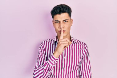 Gündelik kıyafetler giyen genç İspanyol adam parmakları dudaklarında sessiz olmak istiyor. sessizlik ve gizli konsept. 