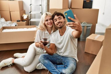 Genç ve güzel bir çift kırmızı şarapla kadeh kaldırıyor ve yeni evlerinde selfie çekiyorlar.