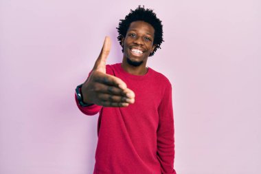 Genç Afro-Amerikan adam günlük kıyafetler giyip gülümseyerek dostça el sıkışarak selamlama ve hoş geldin diyor. başarılı iş. 