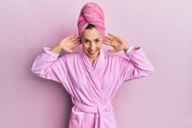 Duş başlığı ve bornoz takan genç sarışın kadın gülümsüyor kulakları parmaklarıyla çekiyor, komik bir jest. deneme sorunu 