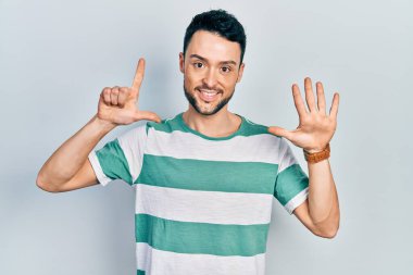 Gündelik kıyafetler giyen genç İspanyol adam yedi numarayı gösterip işaret ederken kendinden emin ve mutlu bir şekilde gülümsüyor.. 