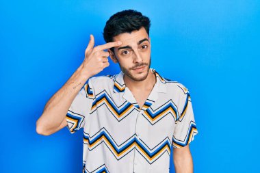 Alnındaki sivilceden mutsuz olduğunu gösteren günlük kıyafetler giyen genç İspanyol adam, siyah başlıklı çirkin enfeksiyon. sivilce ve deri problemi 