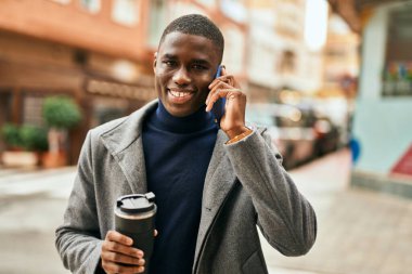 Genç Afrikalı Amerikalı adam akıllı telefonda konuşuyor. Şehirde kahve içiyor.
