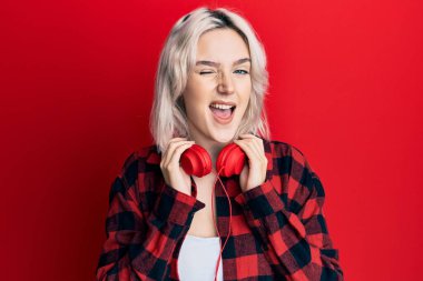 Kulaklıkla müzik dinleyen genç sarışın kız kameraya seksi bir ifadeyle bakıyor, neşeli ve mutlu bir yüzle.. 