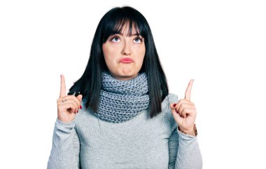 Genç Latin kökenli, kışın atkı takan kadın üzgün ve üzgün görünüyor, parmaklarıyla yön gösteriyor, mutsuz ve depresyonda.. 