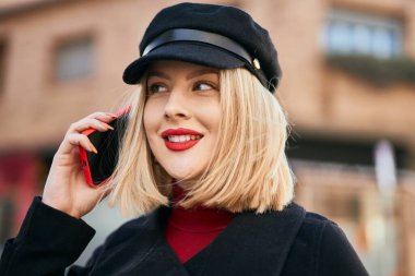 Genç sarışın kadın gülümsüyor. Şehirdeki akıllı telefondan konuşuyor..