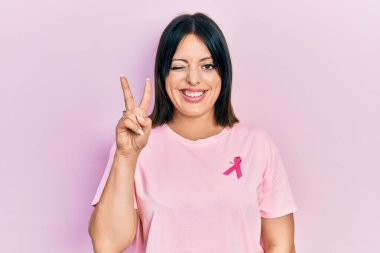 Tişörtüne pembe kanser kurdelesi takmış genç İspanyol kadın kameraya gülümseyip parmaklarıyla zafer işareti yapıyor. İki numara.. 