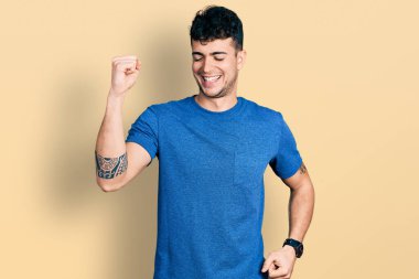 Gündelik tişört giyen genç İspanyol adam mutlu ve neşeli dans ediyor, gülümsüyor rahat ve kendinden emin bir şekilde müzik dinliyor. 