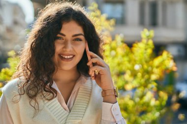 Genç İspanyol kadın gülümsüyor. Şehirdeki akıllı telefondan konuşuyor..