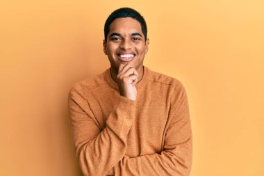 Sıradan bir süveter giyen genç, yakışıklı İspanyol adam kameraya kollarını kavuşturup gülümseyerek ve çenesini kaldırarak bakıyor. Olumlu düşünmek. 