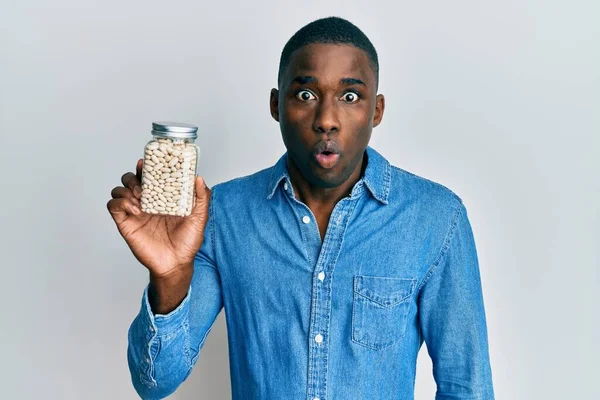Joven Hombre Afroamericano Sosteniendo Frasco Frijoles Asustado Sorprendido Con Boca — Foto de Stock