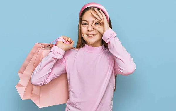 아름다운 갈색의 소녀가 쇼핑백을 행복하게 미소를 손으로 손가락을 확인하는 사인을 — 스톡 사진