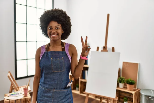 若いですアフリカ系アメリカ人女性とともにアフロヘアでアートスタジオショーや指の数2を指摘しながら 自信と幸せ笑顔 — ストック写真