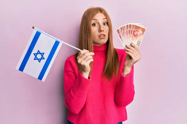 年轻的爱尔兰女人拿着以色列国旗和先令钞票 脸上流露出茫然困惑的表情 怀疑概念 — 图库照片