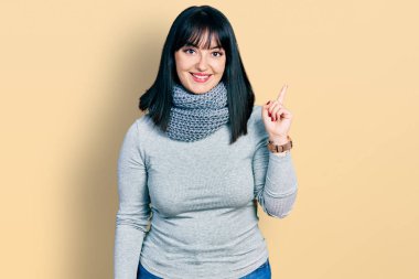 Genç İspanyol artı cüsseli bir kadın. Yüzünde kocaman bir gülümseme olan eşarp takıyor. Parmağıyla kameraya bakıyor.. 