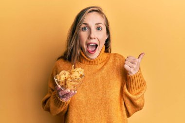 Genç, sarışın bir kadın elinde makarna kasesiyle başparmağını kaldırmış, ağzı açık gülümsüyor. 