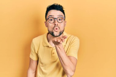 Gündelik kıyafetler giyen ve gözlüklü genç İspanyol adam kameraya bakıp havada el sallayarak öpüşüyor ve çok güzel ve seksi. aşk ifadesi. 