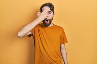 Sakallı, sıradan sarı tişörtlü, beyaz bir adam. Şoka girmiş, yüzünü ve gözlerini kapamış, utangaç ifadesiyle parmaklarının arasından bakıyor.. 