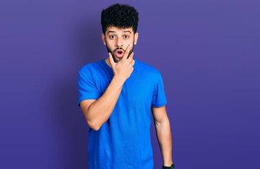 Sakallı, sıradan mavi tişörtlü genç bir Arap. İnançsızlıktan, şaşkınlıktan ve elleri çenesinde şaşkınlıktan büyülenmiş bir ifadeyle bakıyor. 