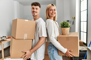 Genç beyaz çift mutlu bir şekilde gülümsüyor. Yeni evlerinde karton kutular tutuyorlar..