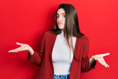 İş ceketi giyen genç esmer, elleri ve kolları havada, kafası karışık bir ifade takınıyor. şüphe kavramı. 