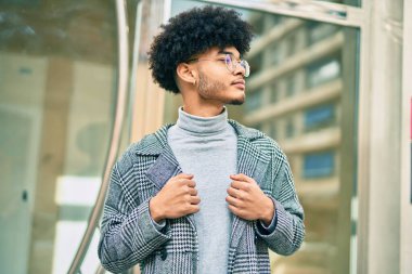 Genç Afro-Amerikan iş adamı ciddi bir ifadeyle şehirde duruyor..