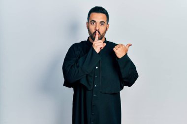 Sakallı, Katolik rahip cübbesi giyen yakışıklı, sessiz olmak isteyen, parmakları dudaklarında, elleri yanda olan yakışıklı bir İspanyol. sessizlik ve gizli konsept. 