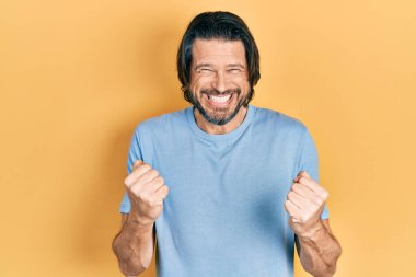 Orta yaşlı, günlük kıyafetler giyen, mutlu ve heyecanlı kolları havada, gülümseyen ve başarı çığlıkları atan bir adam. kutlama konsepti. 