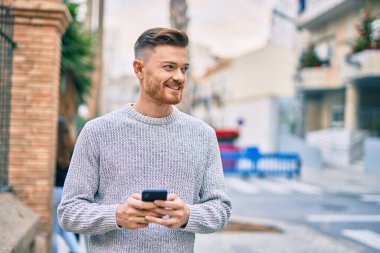 Beyaz adam şehirde akıllı telefon kullanarak mutlu bir şekilde gülümsüyor..