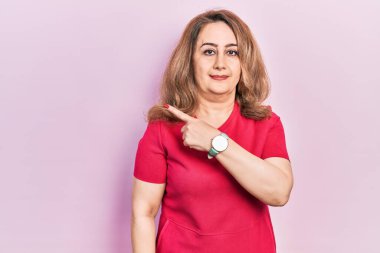 Orta yaşlı beyaz kadın, gündelik giysiler giyip elini kaldırmış, ciddi ve sakin bir yüz ifadesi sergiliyor. 