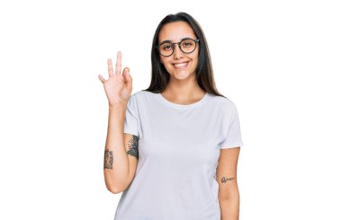 Gündelik beyaz tişört giyen genç İspanyol kadın gülümsüyor ve el ve parmaklarıyla 