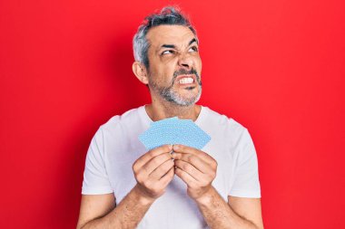 Kartlarla yüzünü kaplayan gri saçlı yakışıklı orta yaşlı bir adam sinirli ve öfkeli çığlıklar atıyor, öfkeyle bağırıyor. öfke ve agresif konsept. 